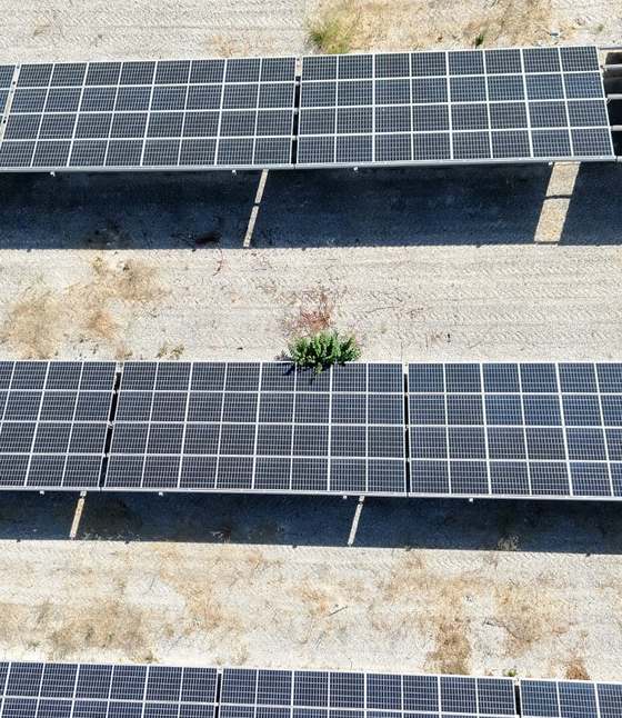 Ripresa aerea di file di moduli fotovoltaici su terreno ghiaioso